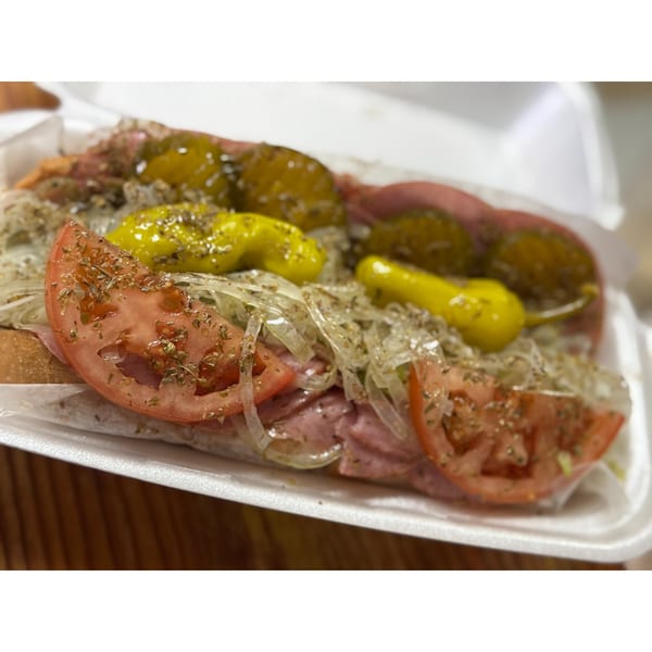 A Nephew's Steak & Hoagy sandwich with sliced tomatoes, onions, and peppers in a white container.