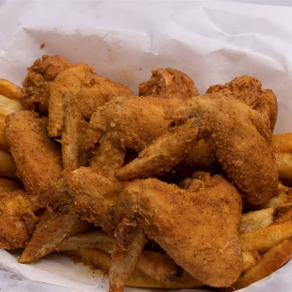 Crispy fried chicken wings and french fries in a white paper-lined basket.