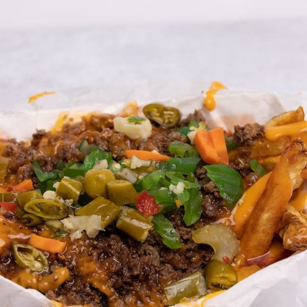 Close-up of loaded fries with ground beef, melted cheese, and various pickled vegetables.