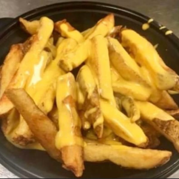A close-up of golden-brown potato wedges generously covered in melted yellow cheese sauce in a black bowl.